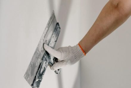 worker in gloves holding putty knife while working at home
